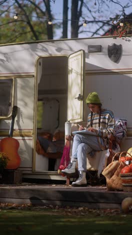 woman drawing outdoors near a campervan in autumn