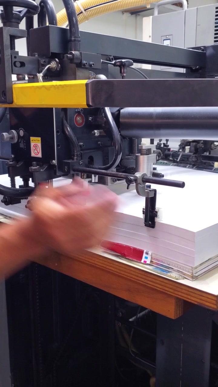 Close-up vertical video professional pressman aligning paper sheets, ensuring precise feeding for automated printing production in a modern graphic facility.