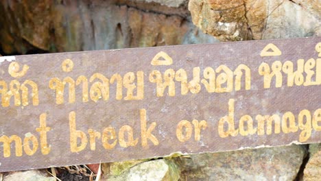 a close-up of a bilingual warning sign at lawa cave, kanchanaburi, thailand, urging visitors not to damage the rocks