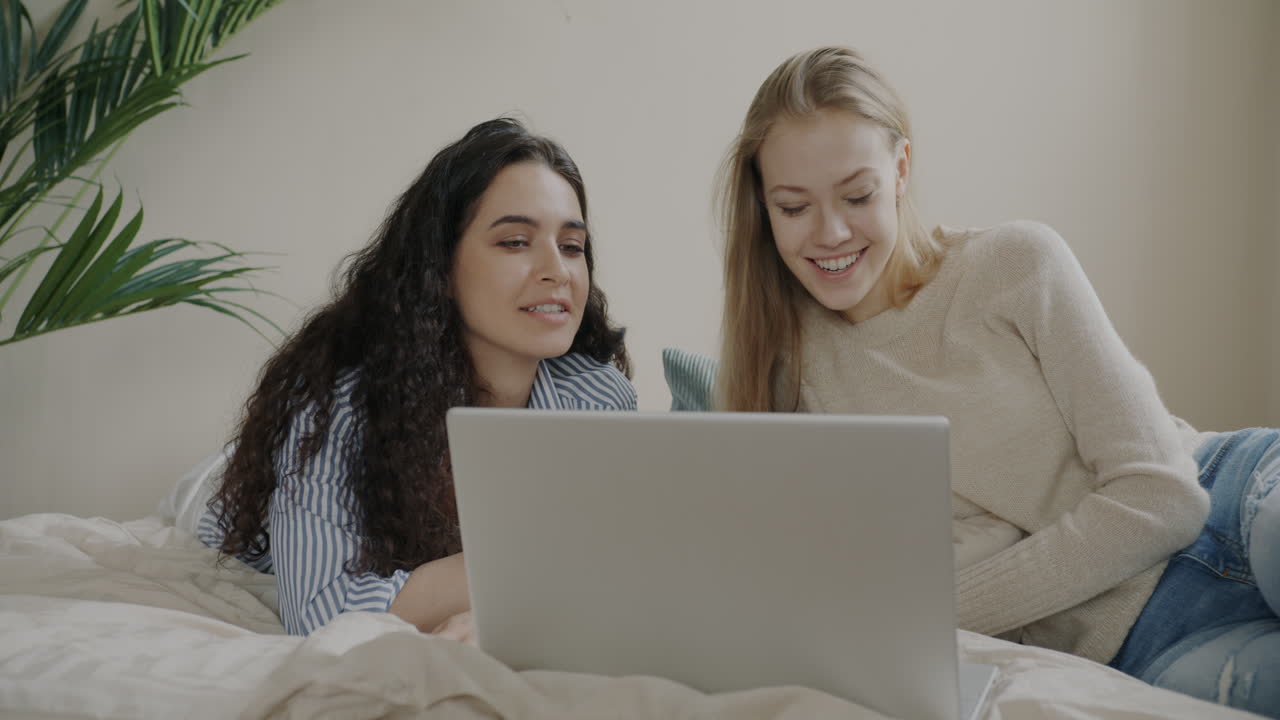 Two friends using a laptop on a bed