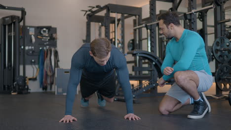 trainer attentively supervises a male client executing spiderman mountain climbers plank exercise