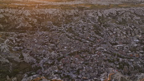 Göreme-Turkey-Aerial-v29-birds-eye-view-flyover-ancient-village-town,-tilt-up-reveals-beautiful-cappadocia-landscape-with-golden-sun-glowing-in-the-sky-at-sunset---Shot-with-Mavic-3-Cine---July-2022