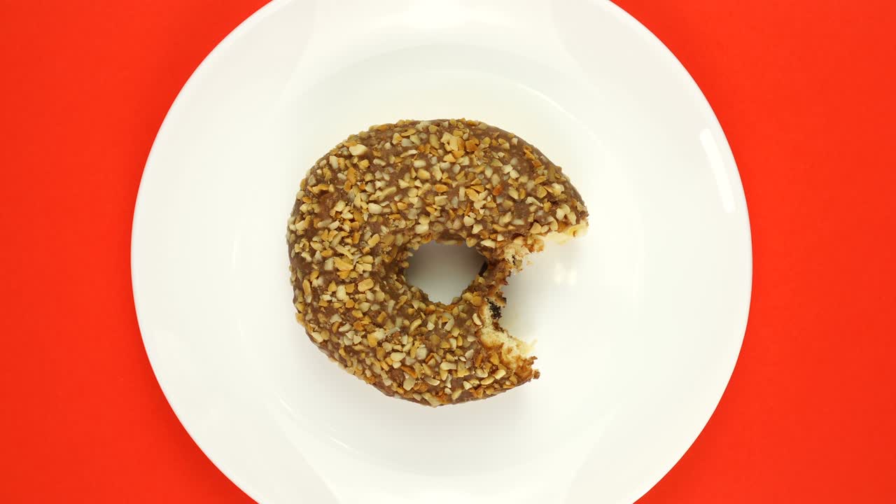 brillante y colorido salpicado mordido rosquilla primer plano disparado girando lentamente en una placa blanca de color.