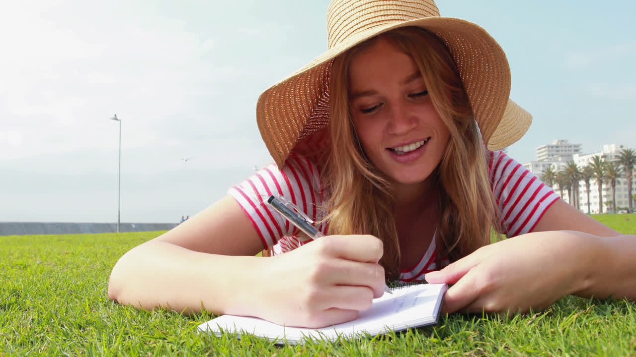 hermosa estudiante joven acostada en el césped estudiando