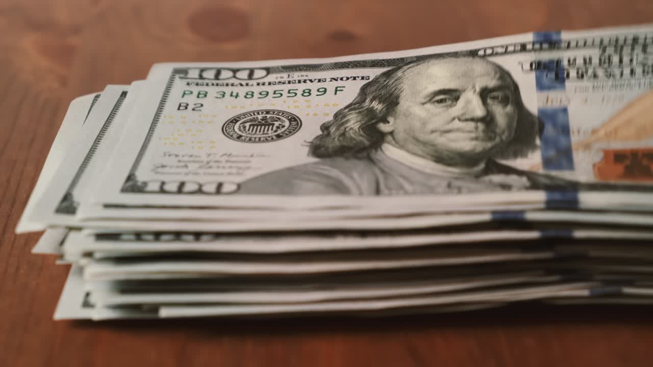 Lapso de tiempo de un fajo de dólares americanos aumentando billete a billete sobre una mesa de madera