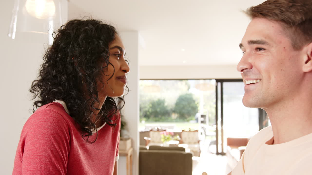 Smiling young multiracial couple looking at each other, enjoying time together indoors, at home
