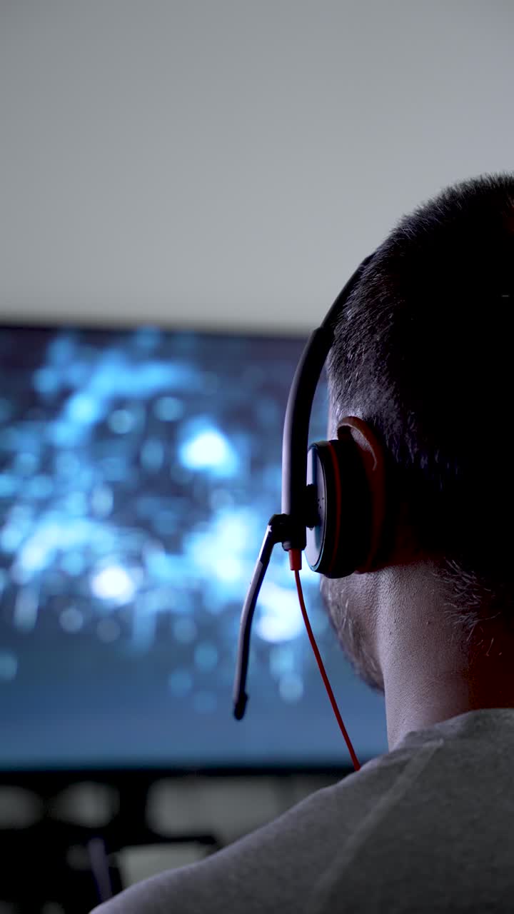 Close-up rear view of a man wearing a headset, facing a blurry blue digital screen, suggesting online communication, gaming, or technical support work