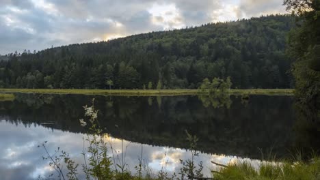 time lapse mountain lake at sunset with green forest of fir trees and fog