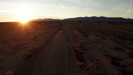 aerial drone chase of white car driving through sunset mojave desert