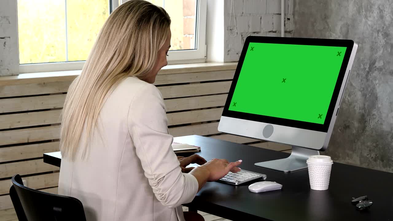 mujer de negocios en vestido sentada en el lugar de trabajo cerca de la ventana y usando la computadora en la oficina. pantalla verde muestra de maquillaje