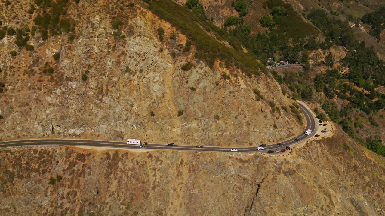 Stunning mountains with little greenery growing on. Road in the middle of rocks at the edge of cliff. Sunny day footage from air.