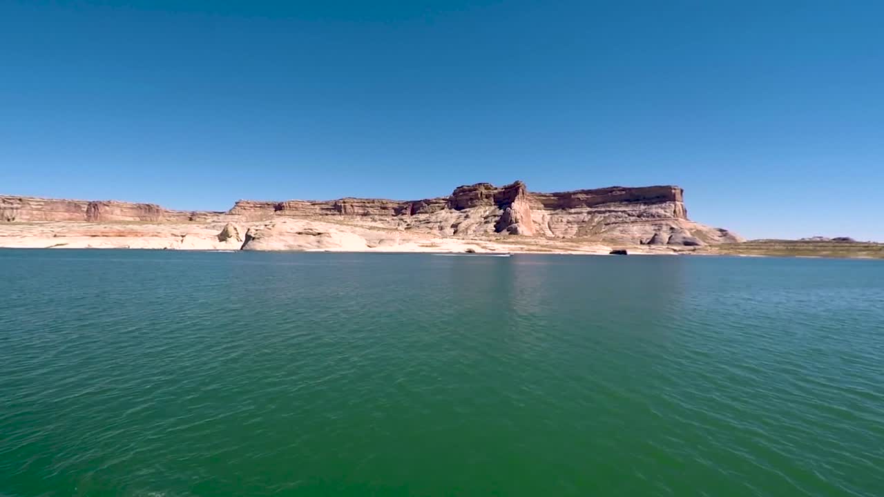 애리조나주 페이지 파웰 호수의 청록색 바다에서 멀리서 본 쾌속정이 사암 버트를 지나