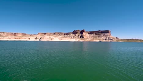 Como-Se-Ve-Desde-Afuera-En-Las-Aguas-Turquesas-Del-Lago-Powell,-Page,-Arizona,-Una-Lancha-Rápida-En-La-Distancia-Recorre-Las-Colinas-De-Arenisca