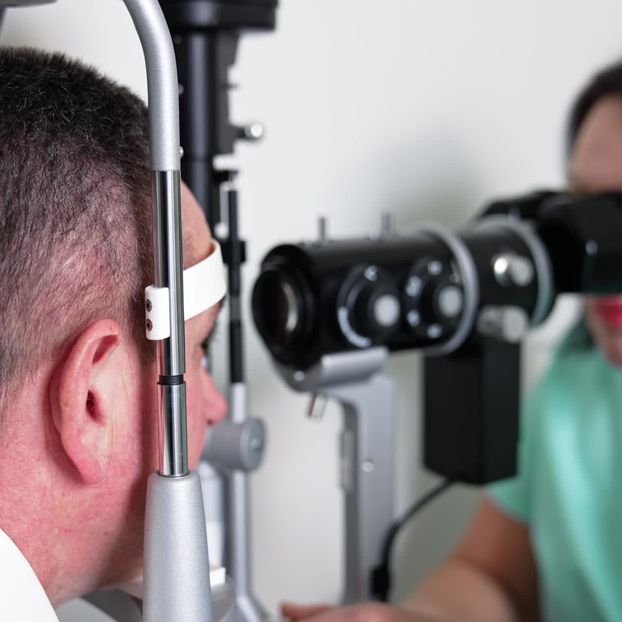 Man goes through eyesight diagnostic at modern equipment. Female doctor checks the patient's eye close up. Blurred backdrop