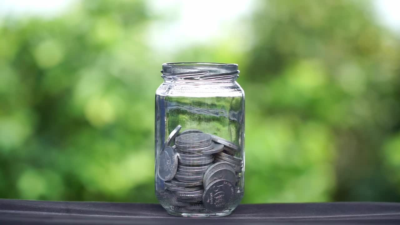 Silver coin falling into a glass with blur green nature background. Business concept, profit and saving.
