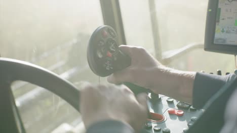 hand controlling joystick inside combine harvester cabin harvesting organic soybeans on sunny day