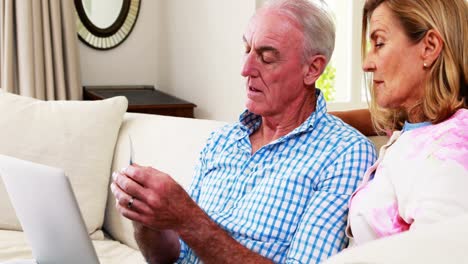pareja de ancianos sonrientes haciendo compras en línea en una computadora portátil en la sala de estar
