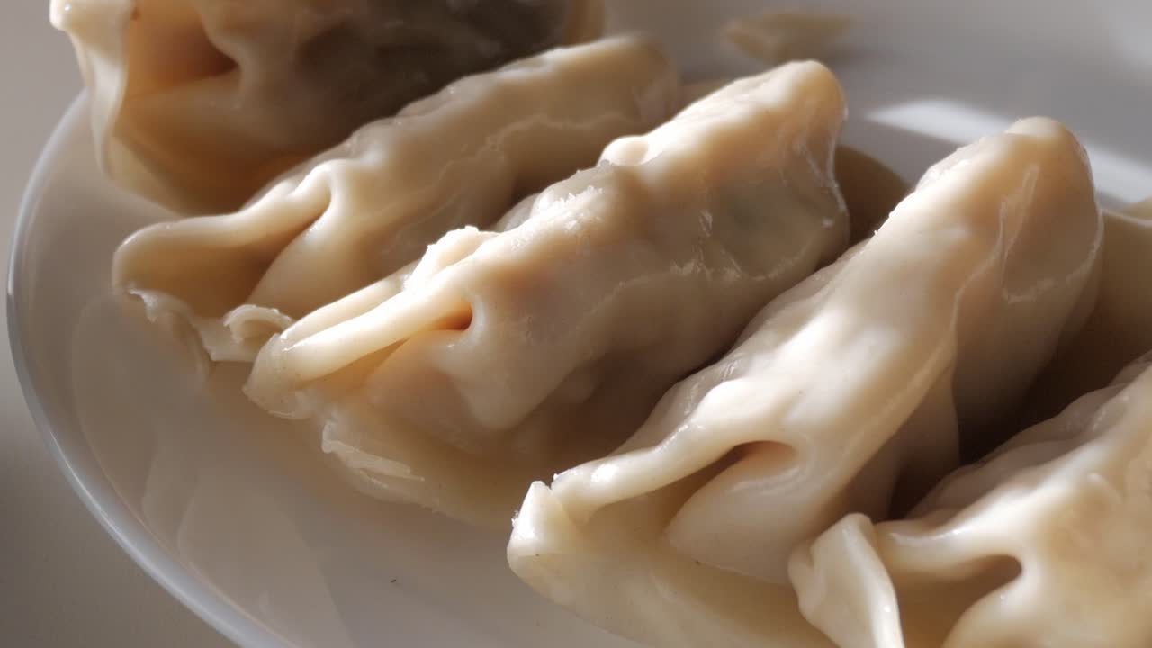 Steamed dumplings on white plate with soy sauce in a traditional ceramic bowl