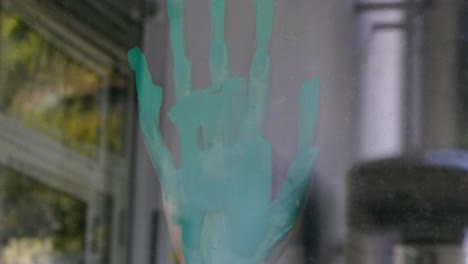 a hand smears green paint on a window glass, view from outside, slight camera movement