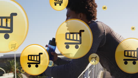 animation of shopping cart icons, tired african american runner taking break and drinking water