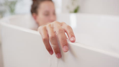Relaxing in bathtub, woman enjoying home day with hand resting on edge