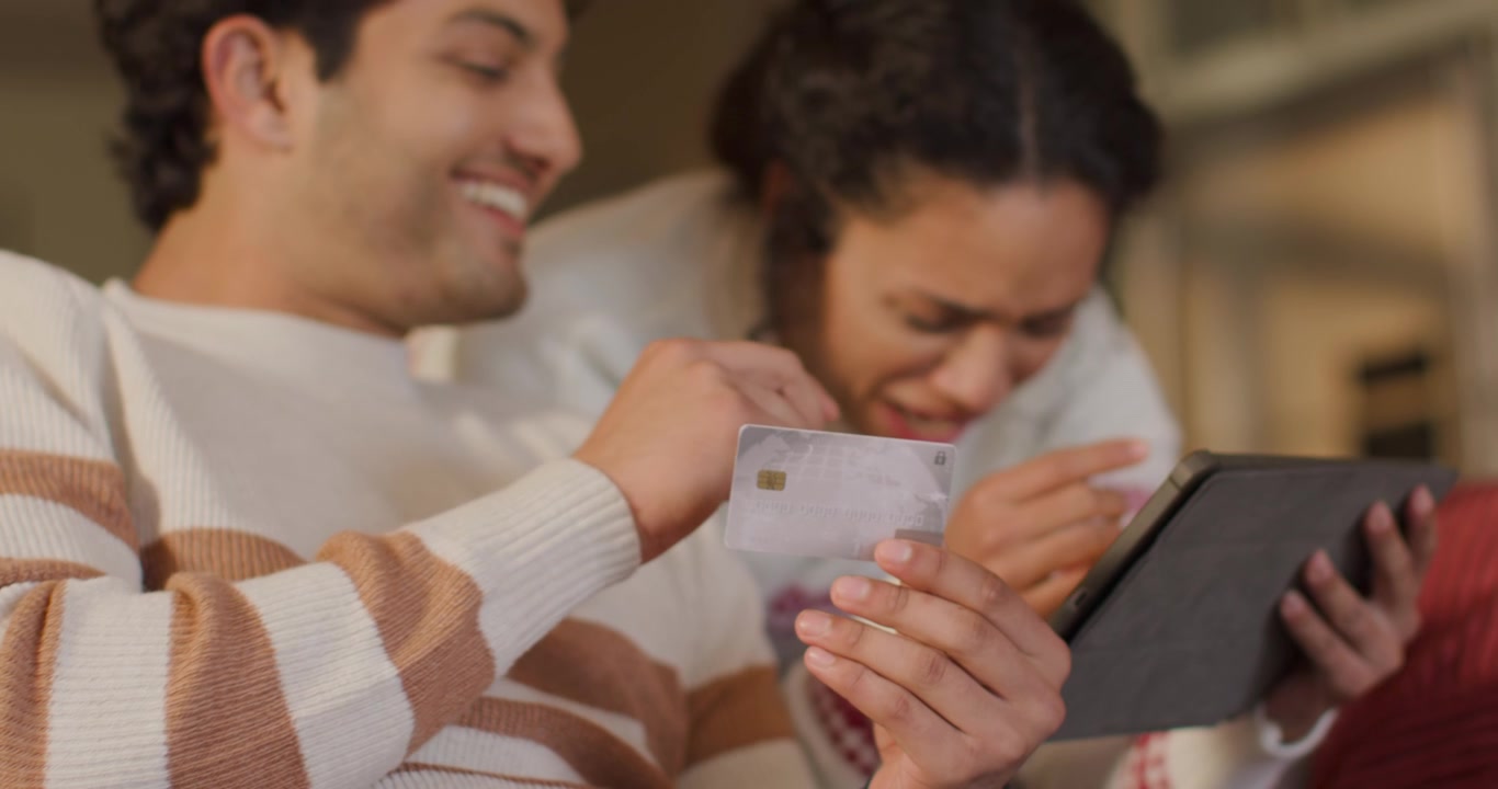 Couple leaning, man holding EMV chip card aligning with tablet on couch while verifying payment