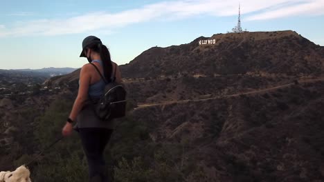 healthy female wearing pandemic mask hiking with dog under famous landmark hollywood sign