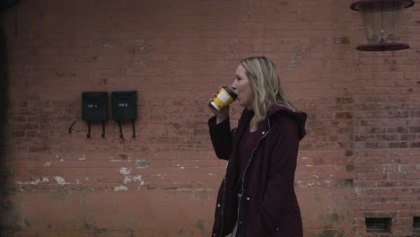 young blonde female smiling and walking down the street with a coffee in hand during the day-1