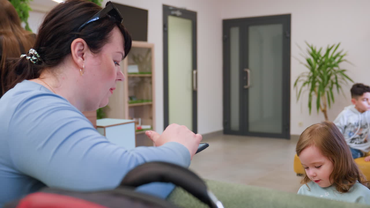 유아에게 휴대폰을 보여주는 엄마의 모습 클로즈업, 부드러운 상호 작용, 호기심 가득한 아이의 시선, 동영상을 보여주는 부모, 따뜻한 실내 조명, 솔직한 가족의 순간, 모바일 교감, 유년 시절의 호기심