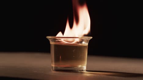 video of lit alcohol in glass with yellow fire flames and copy space on black background