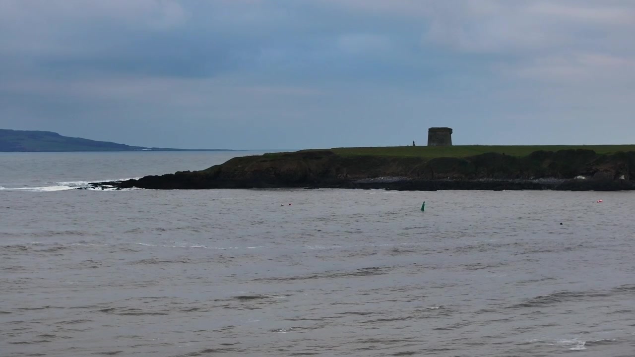 Filmisk vidvinkelbillede af et historisk Martello-tårn på en græsklædt odde i Loughshinny, Nord Dublin, med udsigt over Det Irske Hav