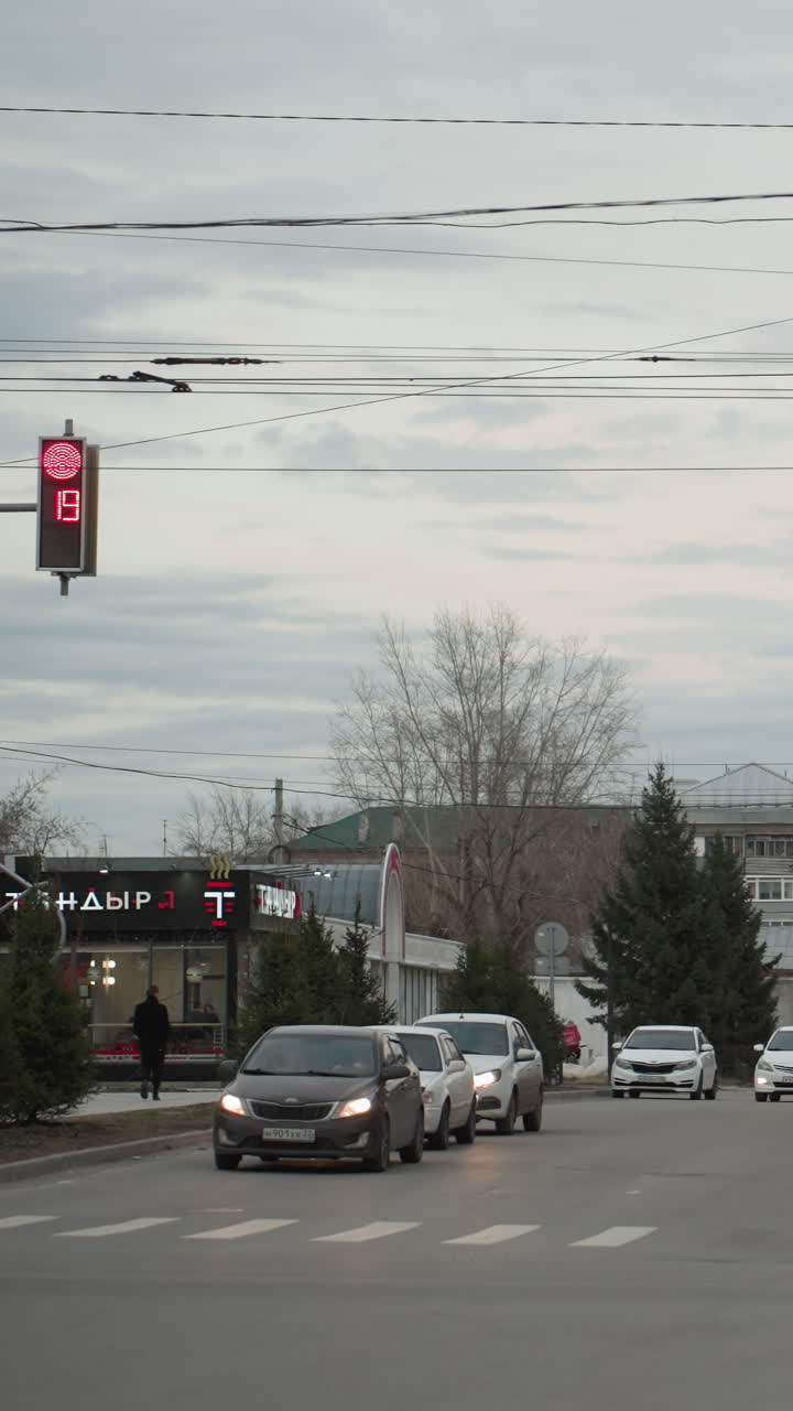 도시 스트리트 뷰는 빨간 신호와 카운트다운을 보여주는 신호등에서 자전거를 타는 자전거 운전자가 등장하며, 자동차가 줄지어 있고, 빨간 건물이 배경입니다.