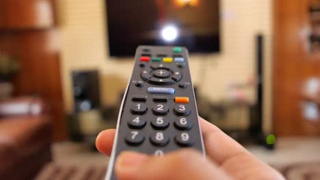 hand holding a tv remote control in a living room