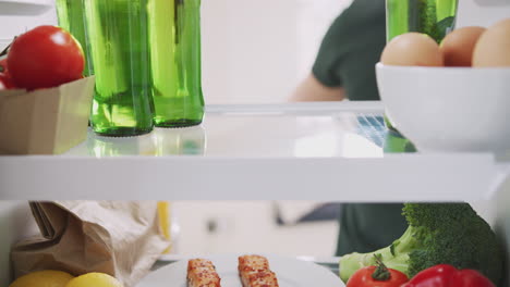 young man reaching inside refrigerator of healthy food for bottle of beer