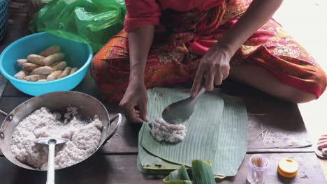 asian woman wrapping portions of food in banana leaf