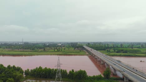 Aerial-view-of-the-flyover-over-farming-land-nearby-the-river,-and-the-canal-after-rain-with-rainy-muddy-water-outside-the-city-in-the-Punjab-region,-INDIA