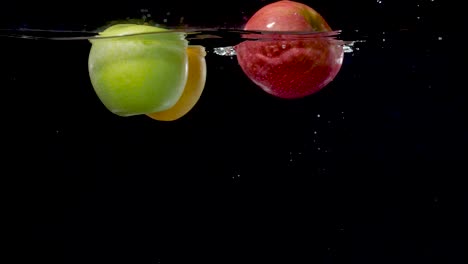 beautiful yellow, green, and red apples floating in water in slow motion