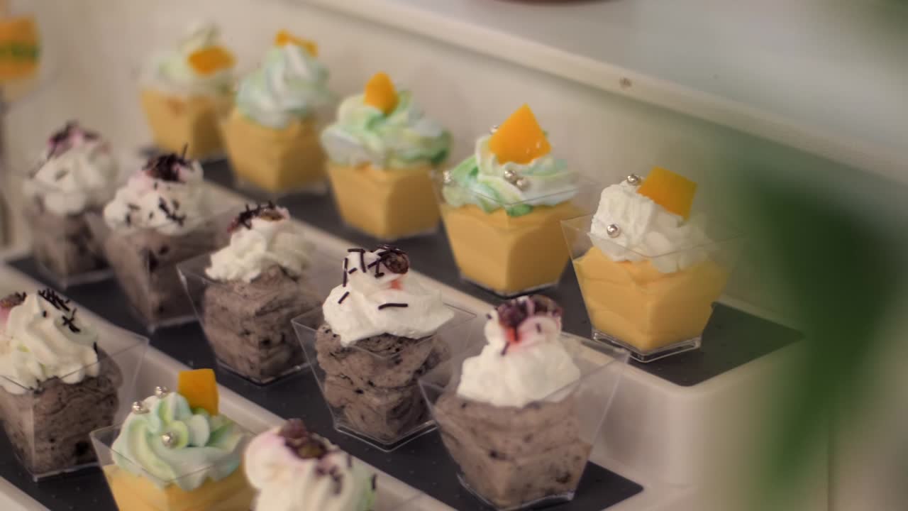 Handheld shot of layered mousse desserts with cream, sprinkles, and fruit toppings.