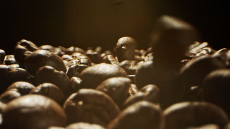 close camera movement through falling fresh coffee beans into a pile of beans laying on a wooden surface