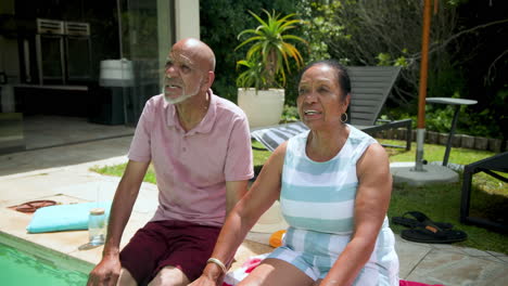 diverse grandparents relaxing by poolside, enjoying sunny day at home garden
