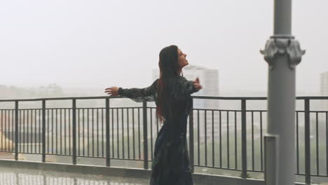 pretty woman turns dancing under heavy rain on viewpoint