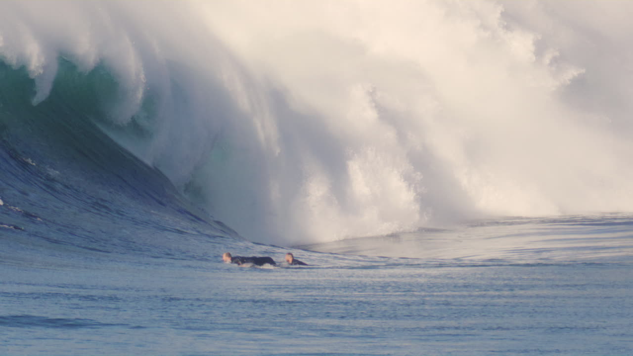 Slow motion view of surfer at golden hour with strong light cast on white raging lip of foam from crashing wave