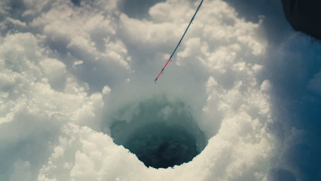 Una canna da pesca sul ghiaccio con un'esca rossa si libra sopra un buco nel ghiaccio. Cattura l'essenza delle attività ricreative invernali. Ideale per promozioni di attività all'aperto o contenuti di sport invernali.