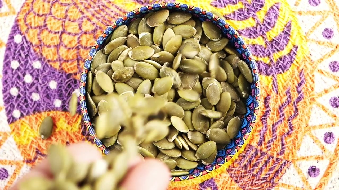 Slowmotion van pompoenpitten die in een kleurrijke kom vallen
