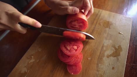 female hand cutting tomato on wooden cutting board