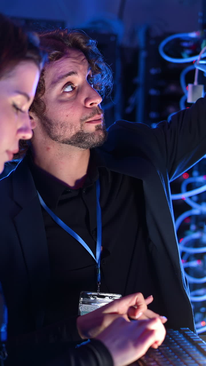 A man and a woman programming in a server room. Vertical