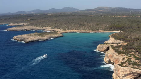 Motorboat-yacht-sailing-into-dark-blue-sea-lagoon-of-Cala-Varques