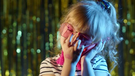 Girl-in-futuristic-glasses-talking-on-mobile-phone-with-mother-in-night-club-with-neon-blue-light