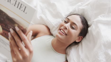 Mujer-Birracial-Feliz-Acostada-En-La-Cama-Leyendo-Un-Libro-En-Casa,-Cámara-Lenta