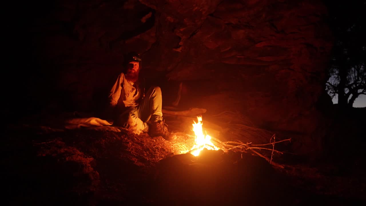 Man camping in a cave with a campfire